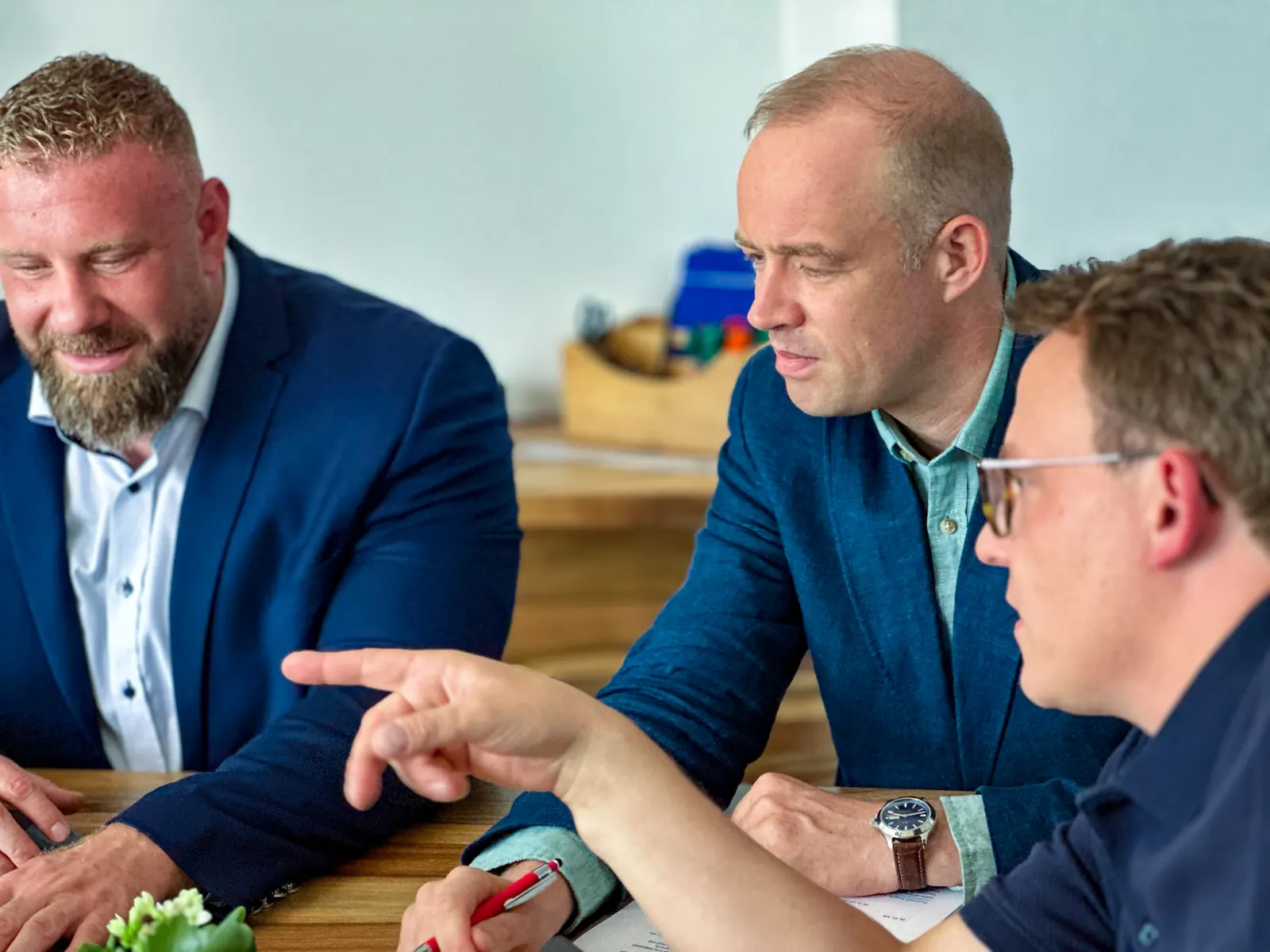 Konstantin Sécrit, Philipp Rowe und Simon Gläve sitzen am Holztisch und besprechen Unterlagen, Simon zeigt auf ein Dokument.